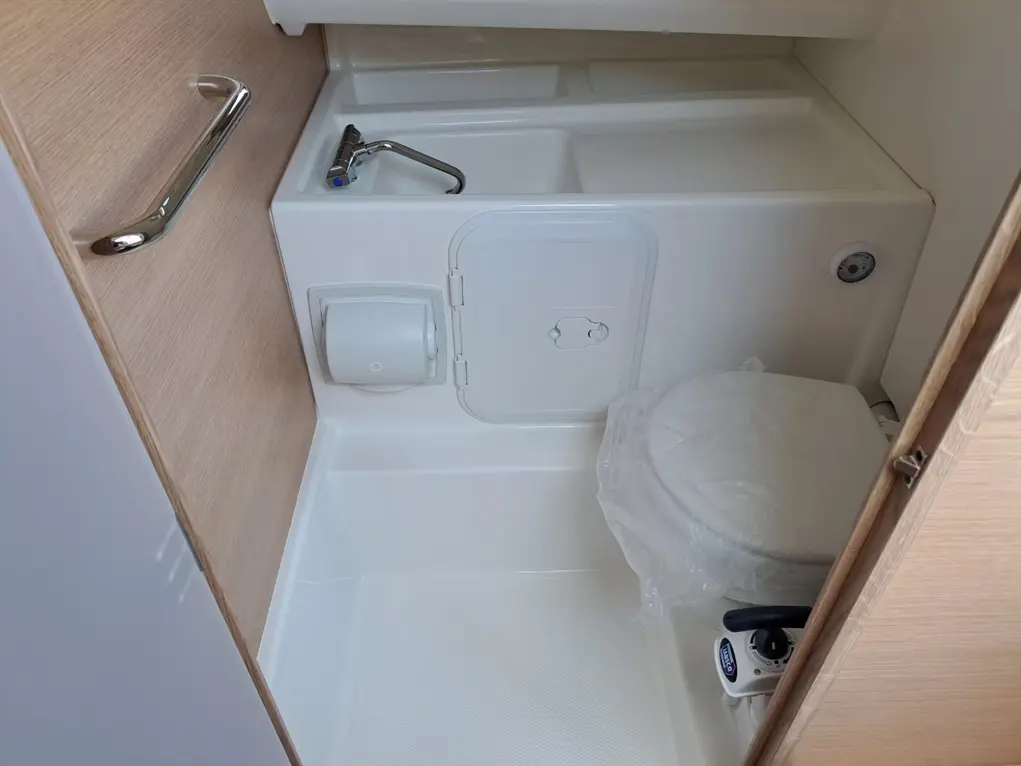 Compact bathroom interior featuring a toilet, wash basin, and wooden paneling, with sanitary packaging still on the toilet.